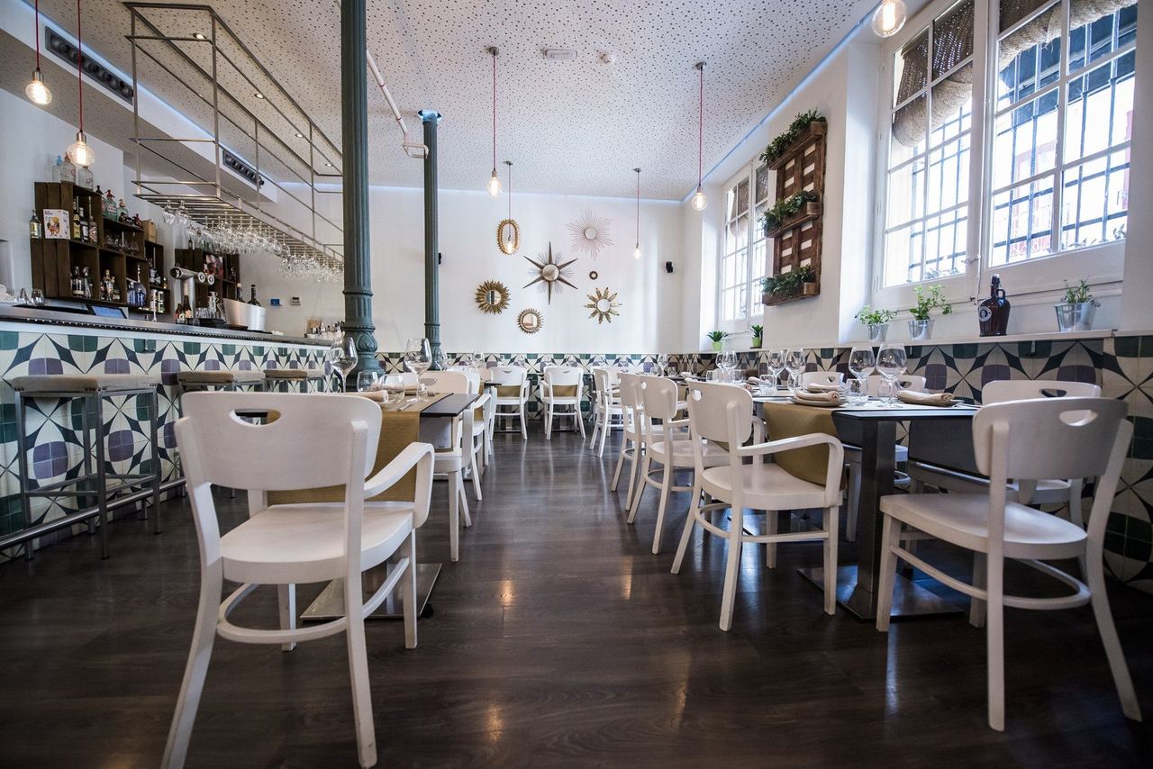 The dining room at Bacira, with white chairs and a tiled bar