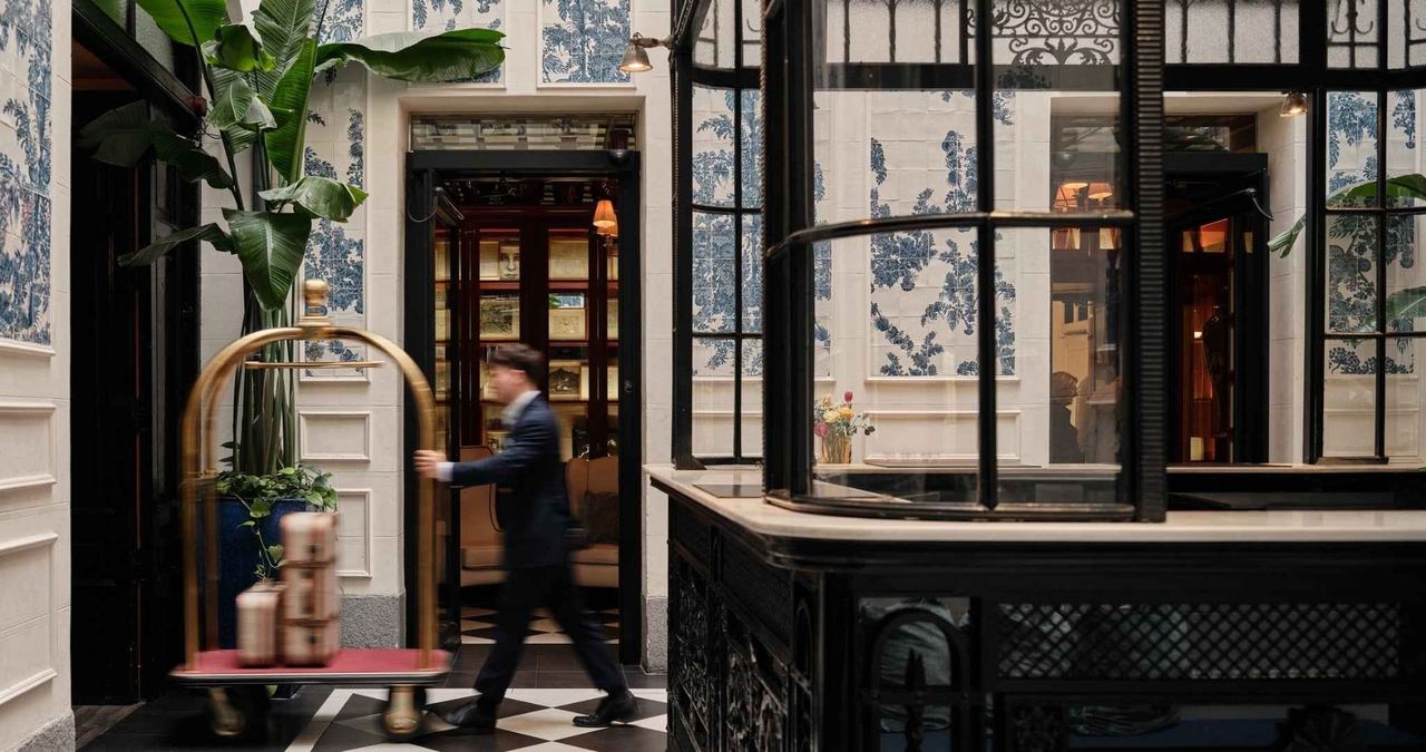 The lobby of Only YOU Boutique Hotel Madrid, with tiled walls, plants and a brass luggage trolley